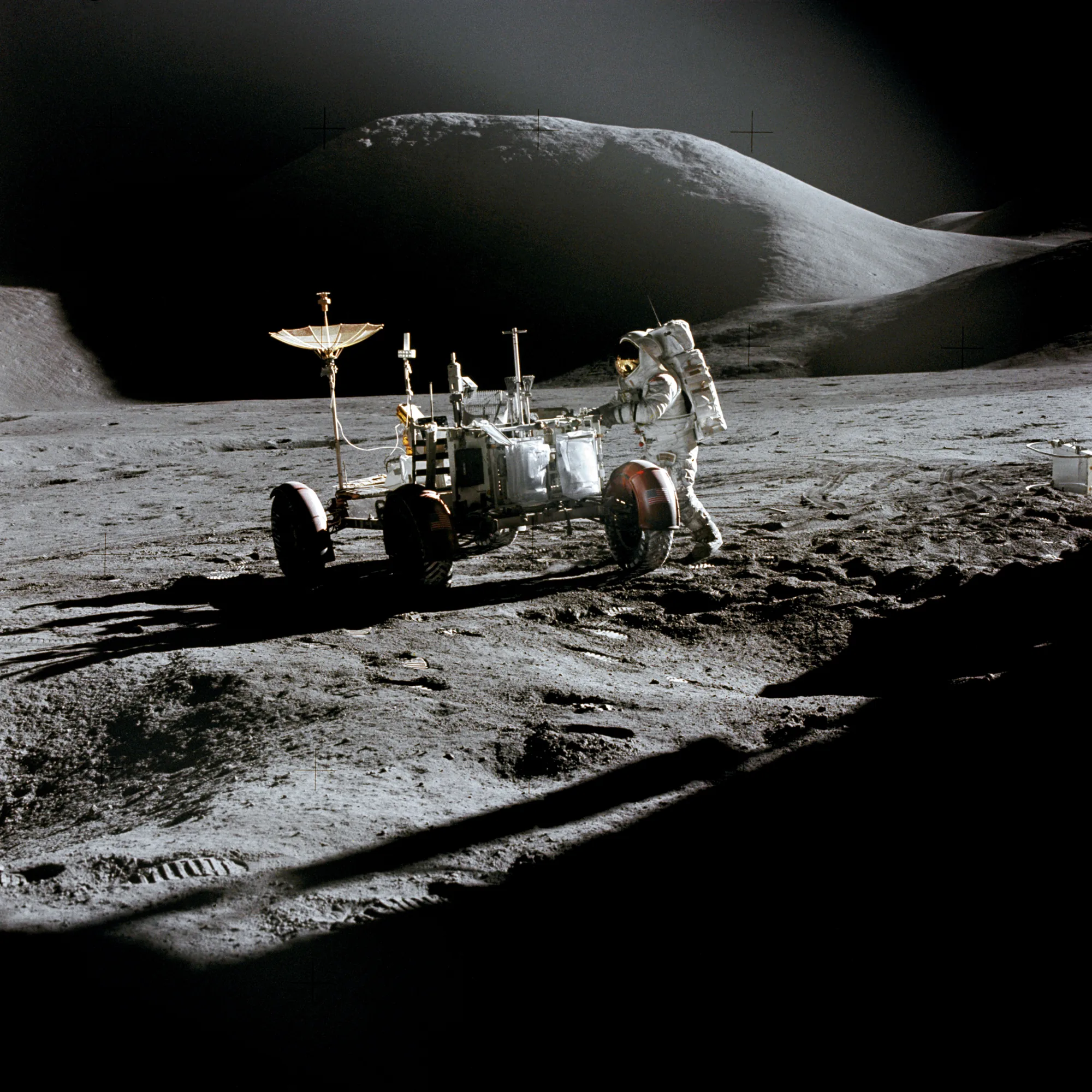 An Apollo 15 astronaut in his spacesuit at the Lunar Roving Vehicle, with Mount Hadley behind